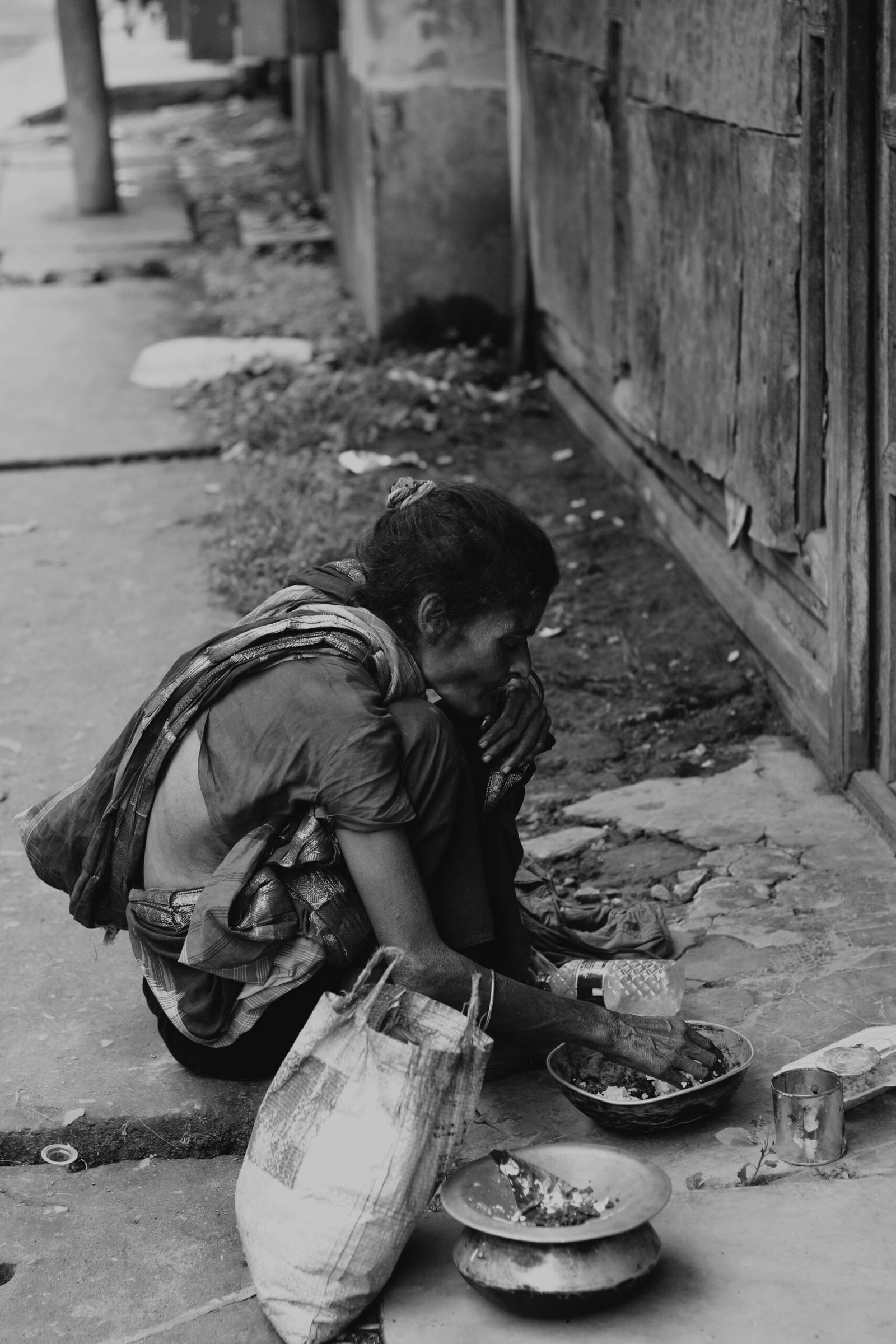 A homeless woman sitting on the street, captured in black and white, conveying poverty and neglect.